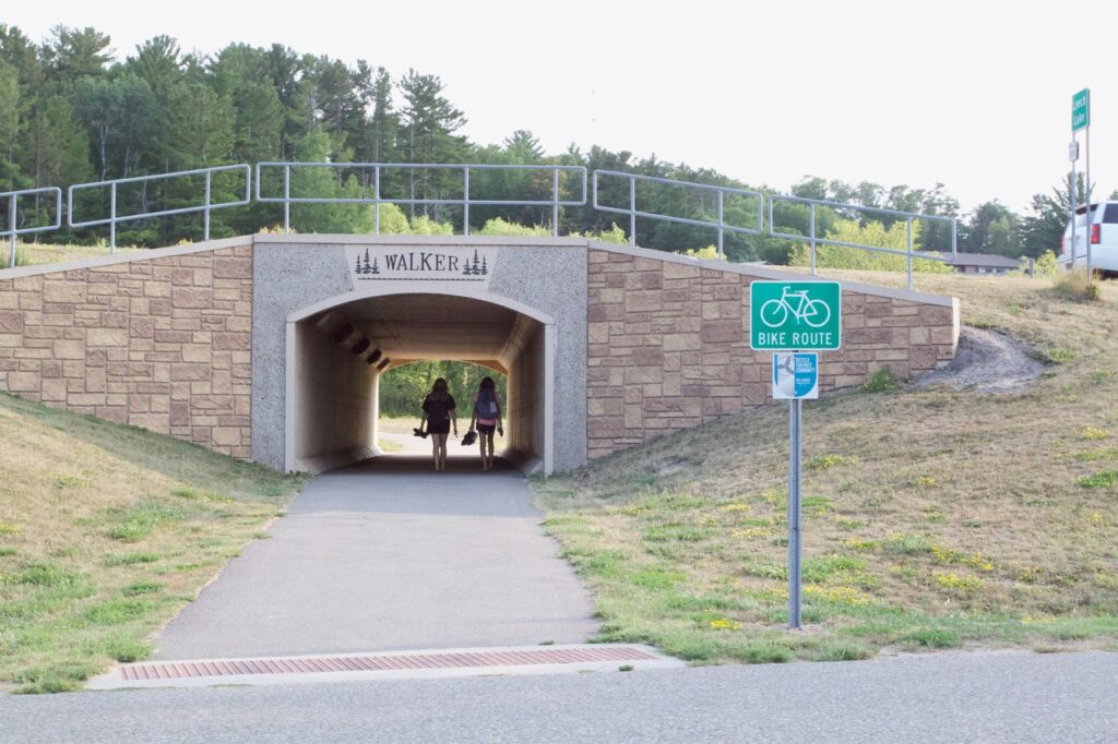Two people walk under a bridge near a bike route.