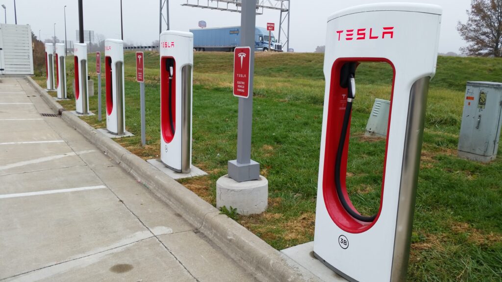 Six Tesla electric vehicle chargers in a line at a gas station parking lot
