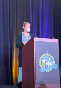 A woman stands at a podium on a conference stage.